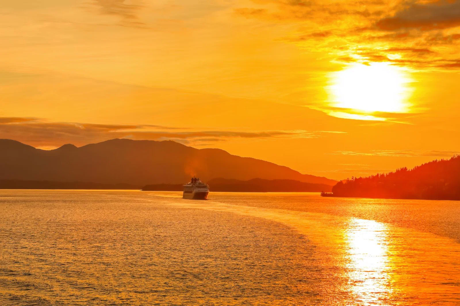 The sun sets over a cruise ship casting yellow light over the water