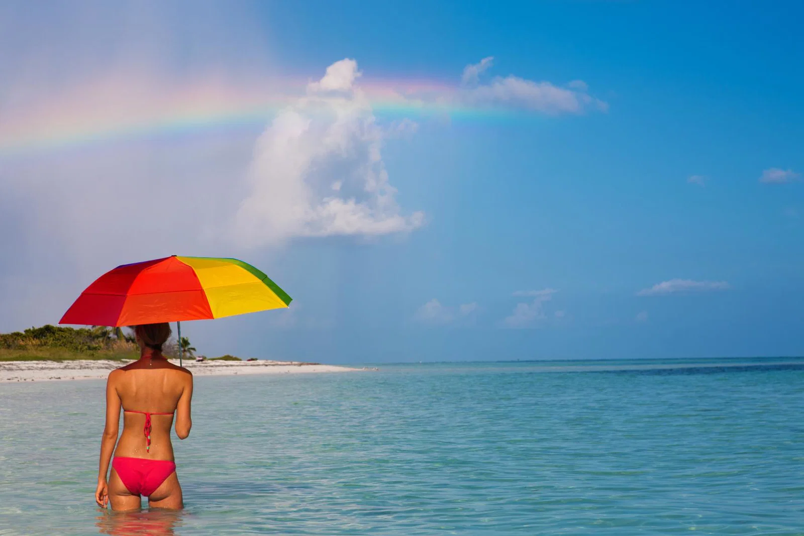 A woman pictured in the sea with an umbrella beneath a rainbow