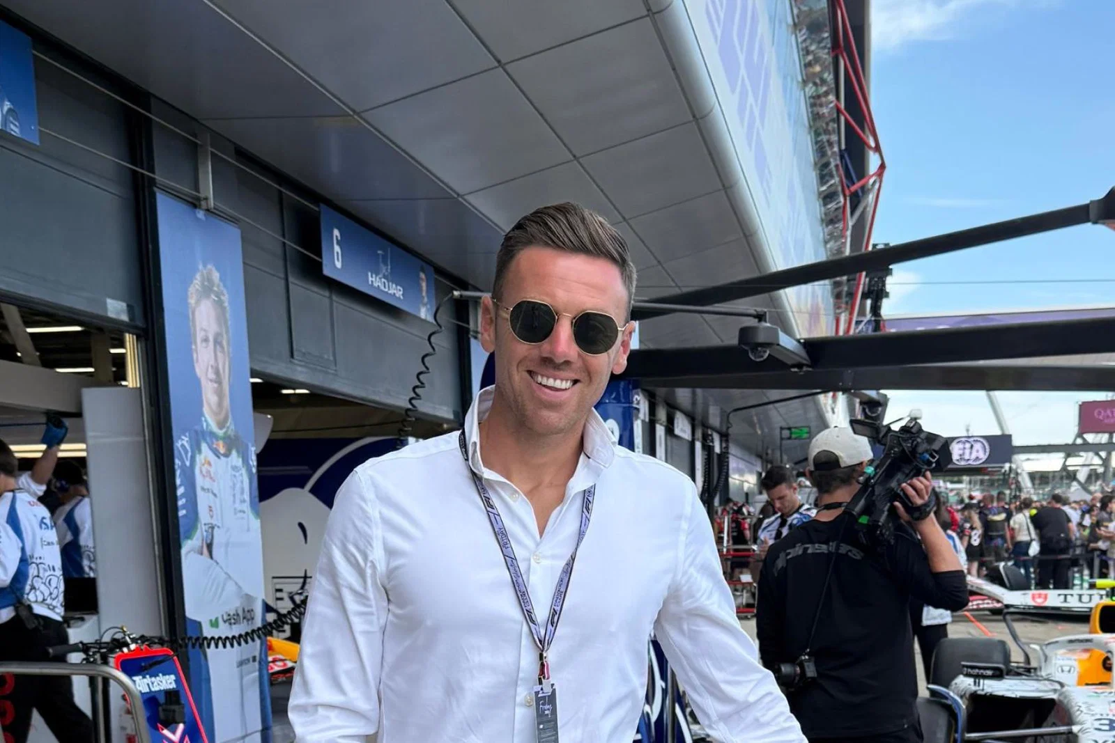 Smiling man wearing sunglasses and white shirt, F1 background 
