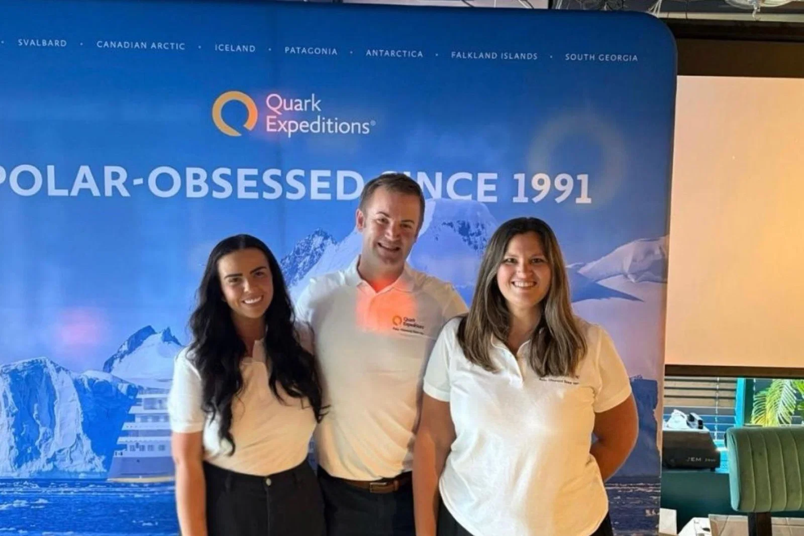 Three people smiling, two women and one man, wearing white t-shirts 
