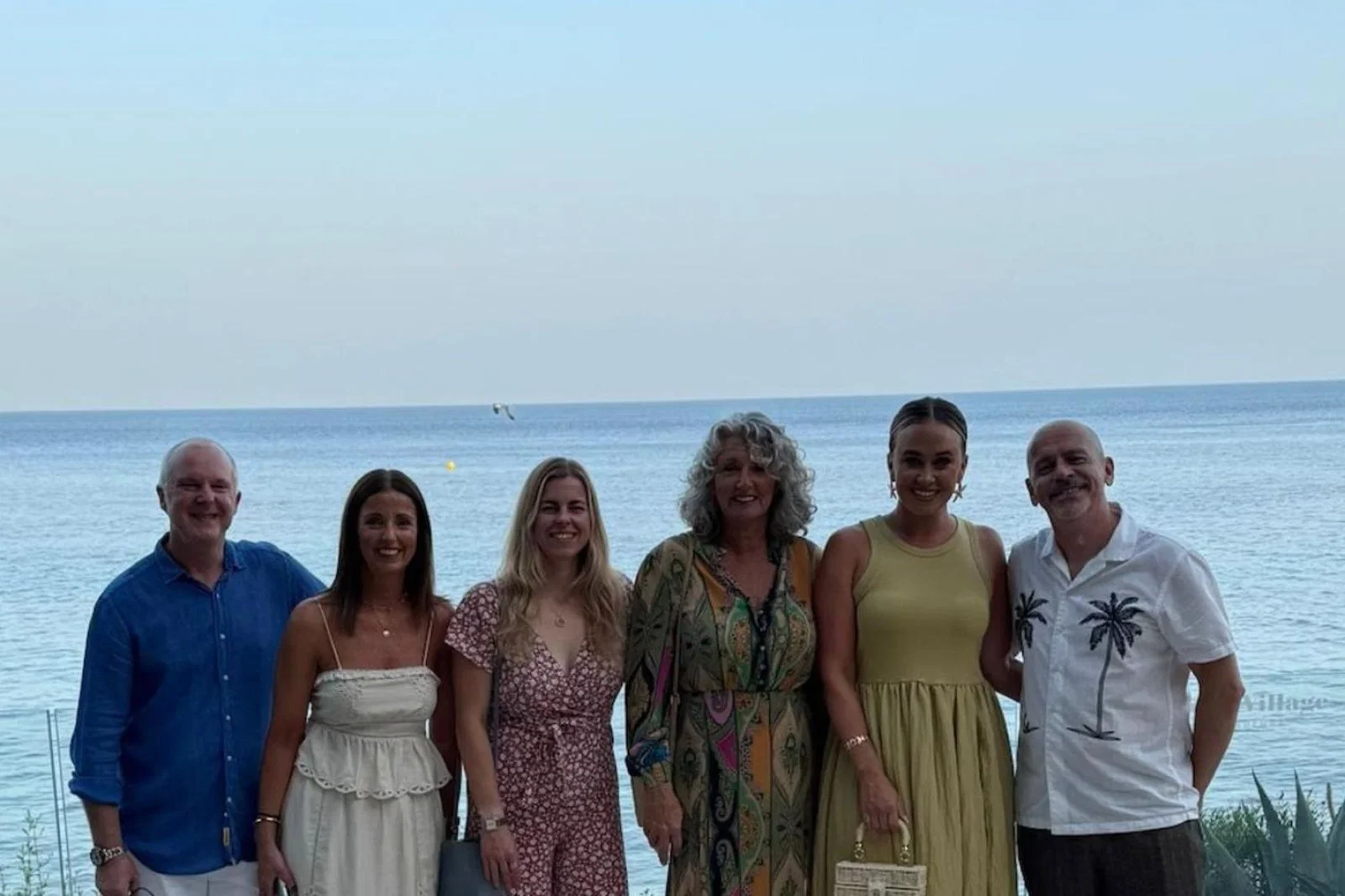 Six people, two men and four women, smiling in front of a beach 