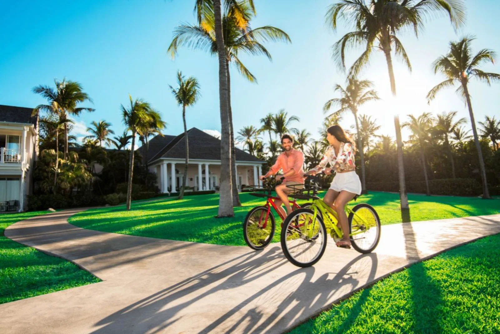 A couple cycling on paved path with grass and palm trees surrounding