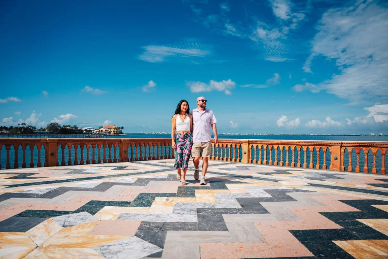 Couple stand in the middle of large mosaic floor with blue sky above