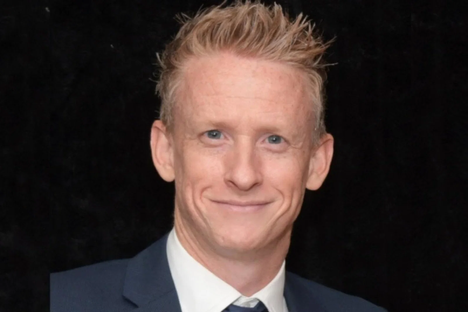 Head shot of white middle-aged man with short blonde hair smiling and wearing suti 