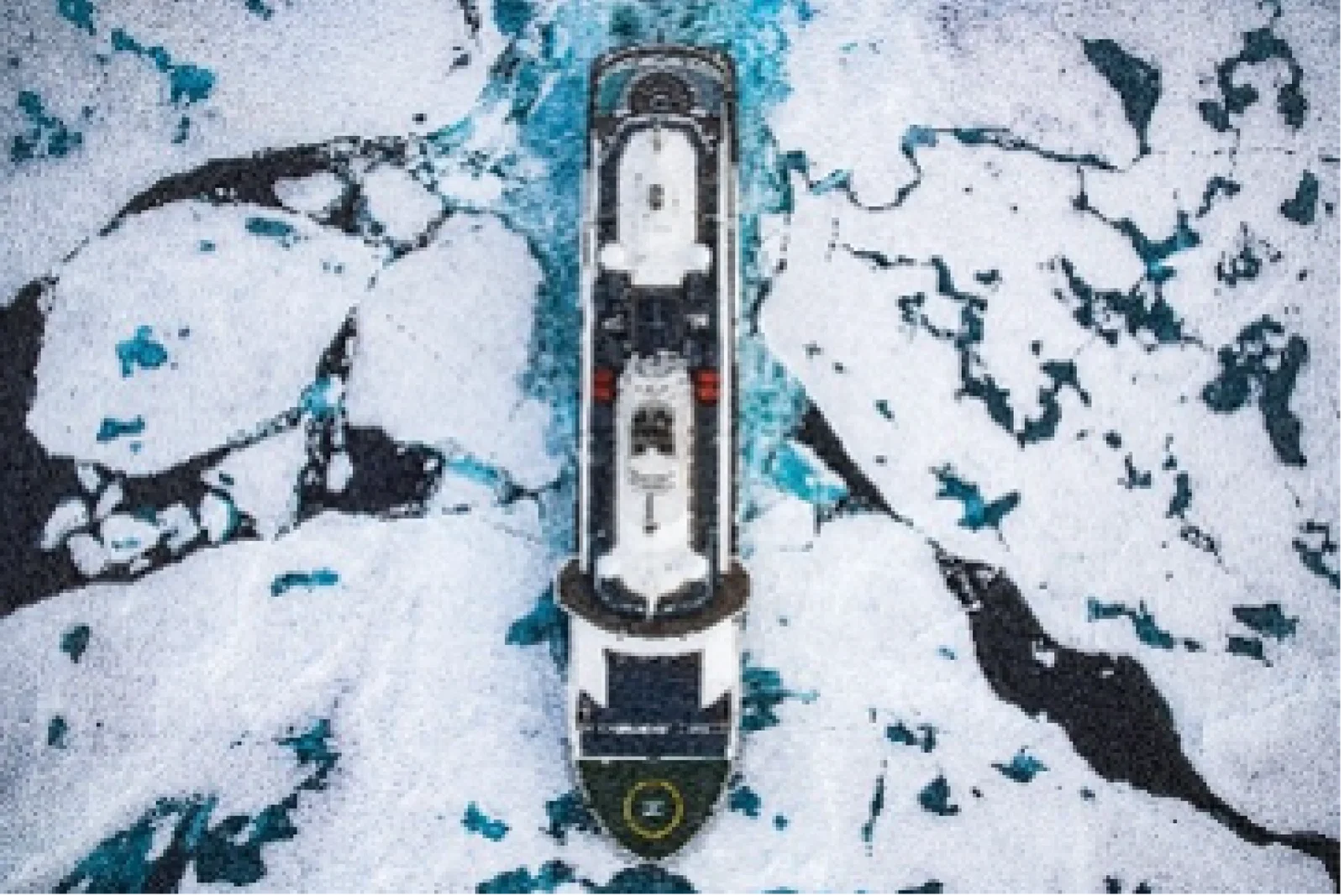 Aerial view of an expedition cruise ship navigating through fractured sea ice in polar waters, its dark hull cutting a path through a mosaic of white ice floes and dark blue-green water below.