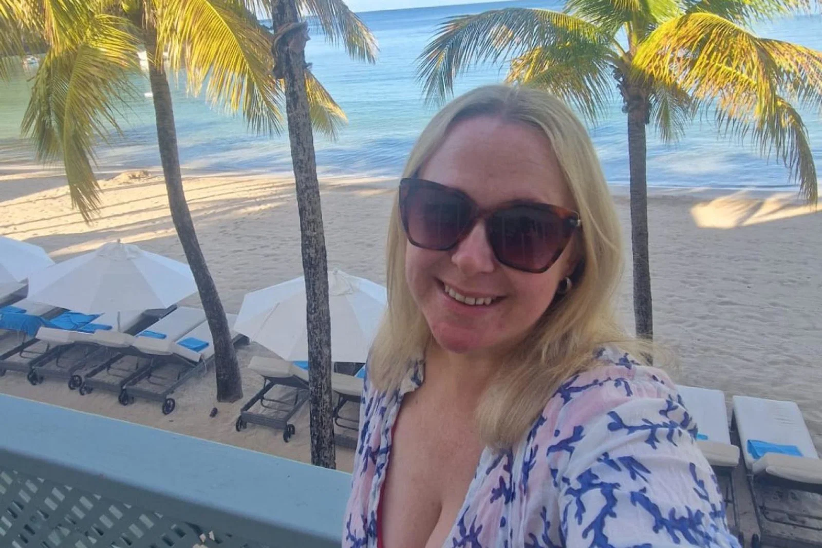 Blonde woman with sunglasses smiling in tropical location   