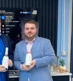 Two young white men standing in suits and holding champagne bottles