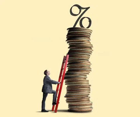 A man looks up as he leans a red ladder against a tall stack of coins that is topped with an interest rate symbol.