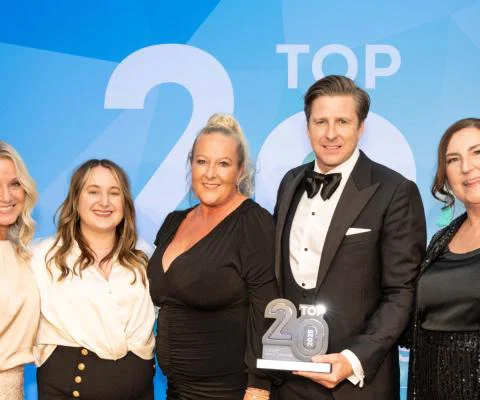 Four women smiling, one man smiling, man is holding trophy statue with 'Top 20' on it. Black tie event. 