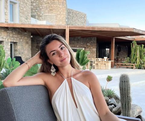 Young white woman with long brown hair sitting on outdoor chair in sunny location