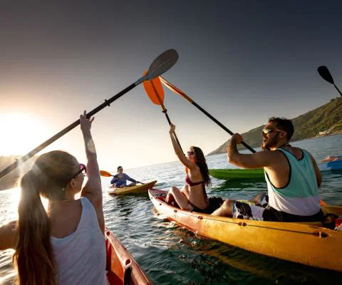 A group out kayaking raise their oars against the sunset