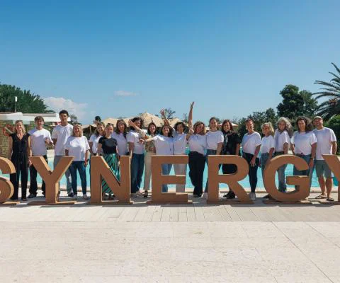 Group of people in front of a large sign that says 'Synergy' 