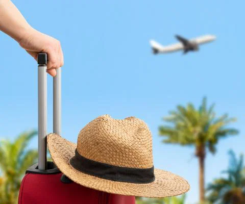A passenger waits with a suitcase and hat as an aircraft takes off