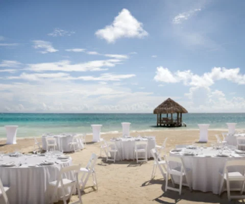 Wedding tables and chairs set up on a white sand beach overlooking the ocean.
