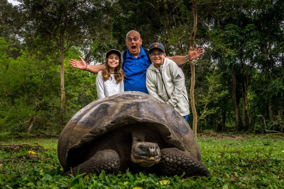 Two children and man smile behind a giant tortoise