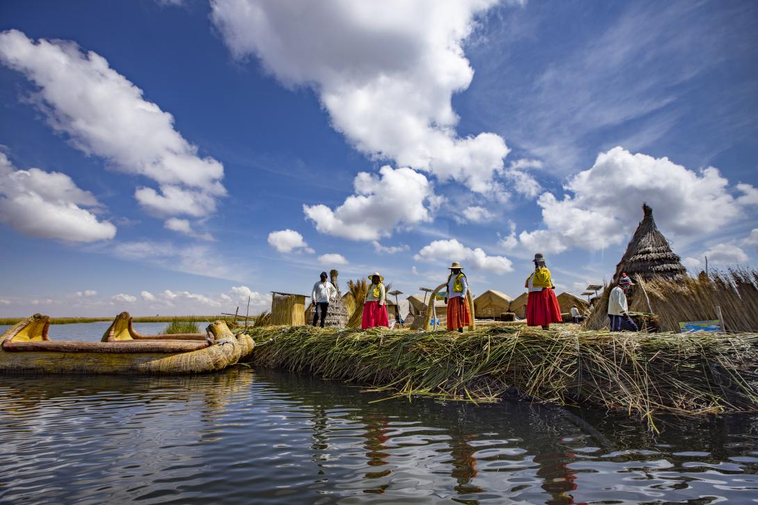 Indigenous people of Peru standing on island made of reeds with a boat