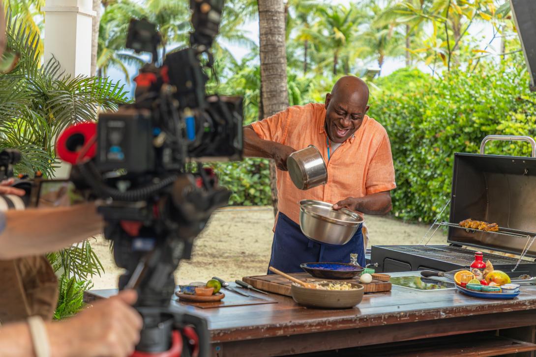 Ainsley Harriott cooking a dish in tropical jungle setting with TV cameras filming