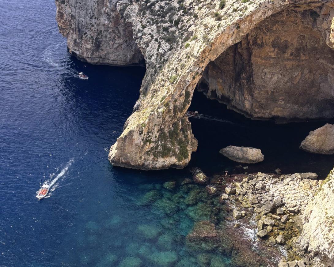 View of beautiful coastline in Malta, with cave and a boat driving over blue ocean water