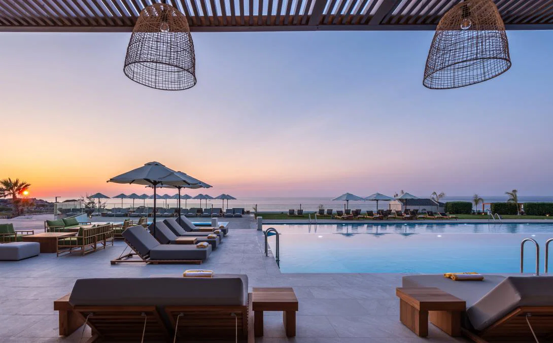 (Credit: Domes Resorts) A hotel pool deck with sunbeds illuminated by a sunset