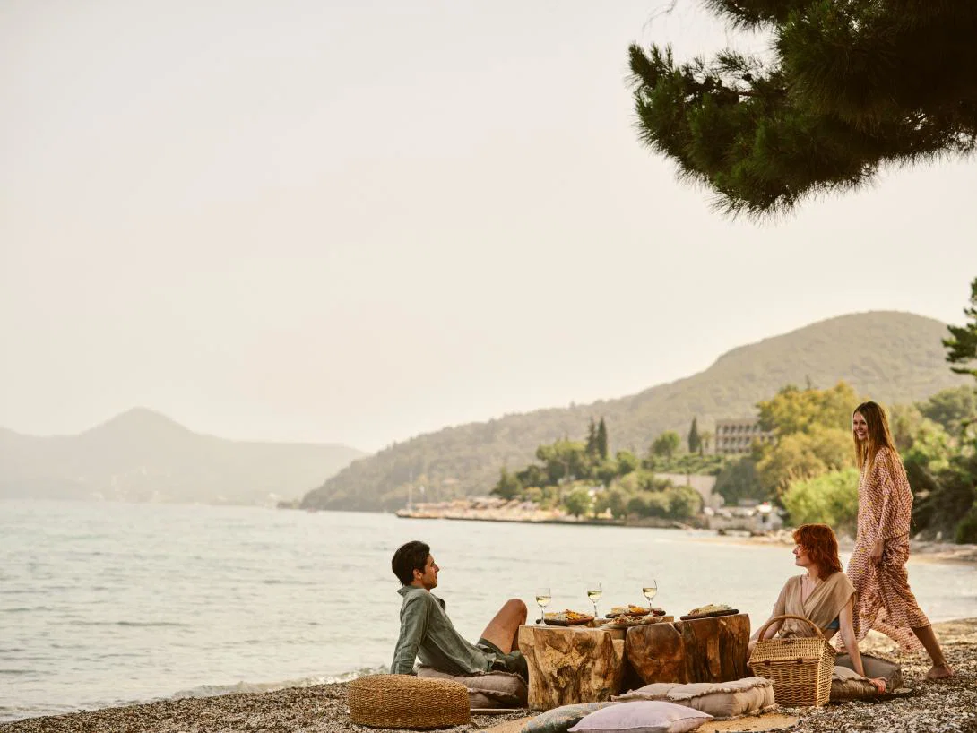 (credit: Mar-Bella Collection) Three adults enjoying a secluded beach picnic with Corfu sea and mountains in background