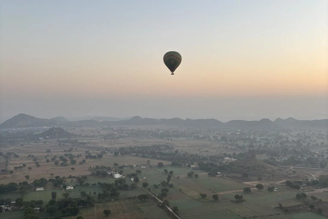 Credit: Jessica Reid A golden sunrise over Rajasthan fields and hills with a hot air balloon in the distance