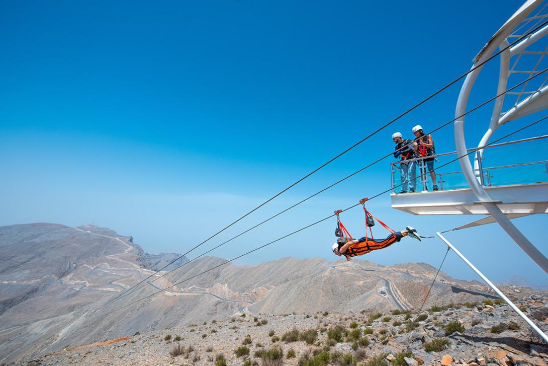(credit: RAKTDA) Person on a lie-flat zipline flying over mountain landscape