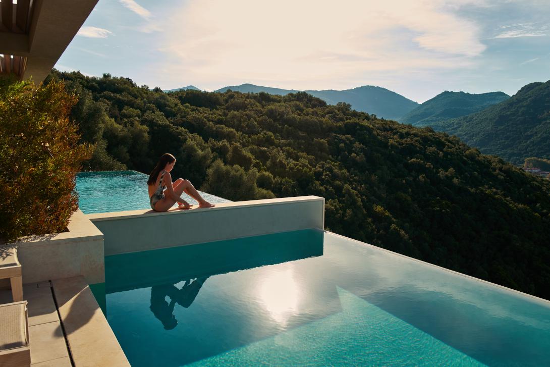 (credit: Mar-Bella Collection) Woman sits on ledge between infinity pools looking out across mountains and coast of Corfu