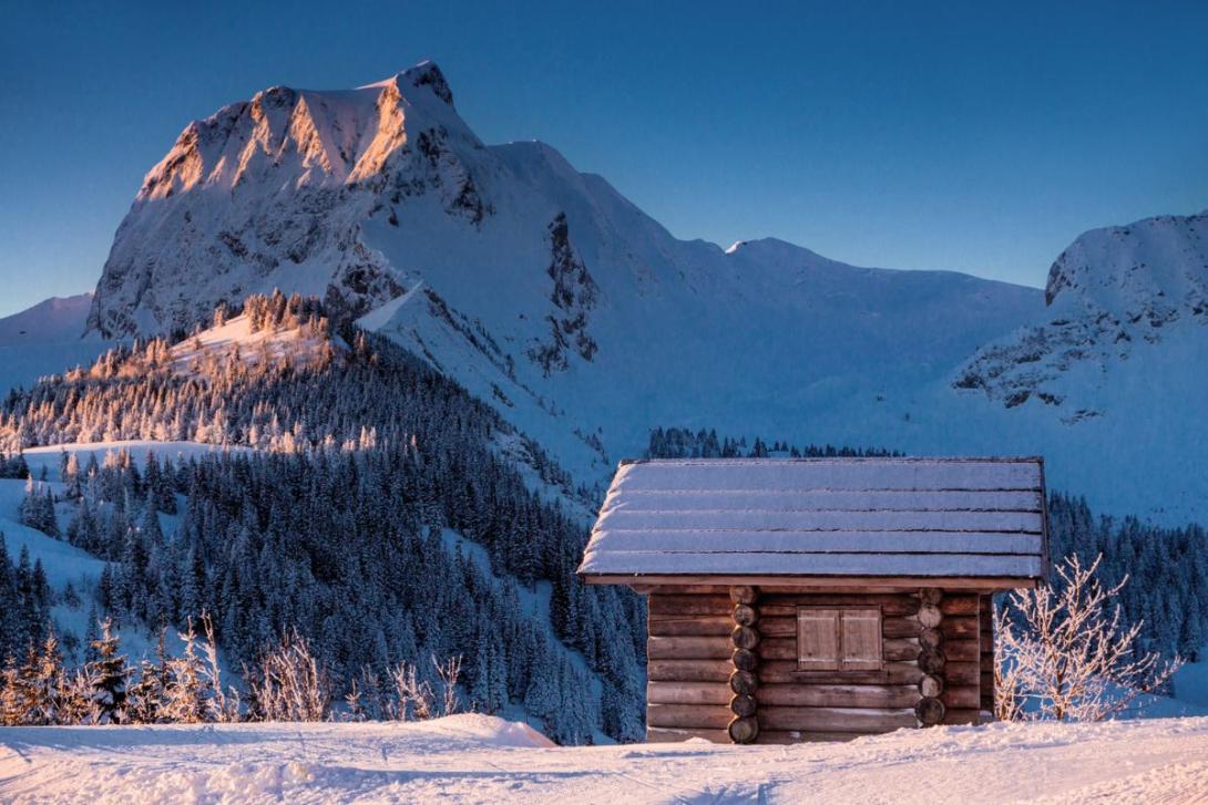 A small wooden snow-dusted house with mountain rising in background