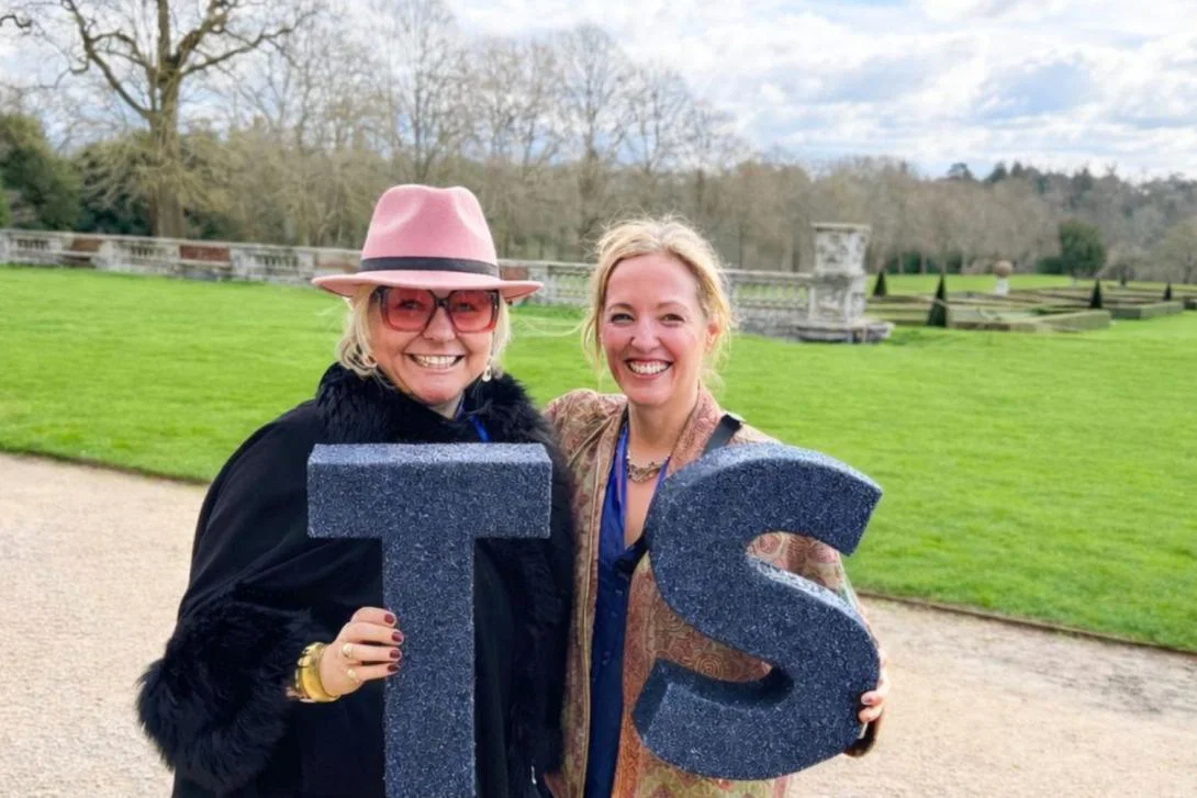 Two women smiling and holding a 'TS' sign