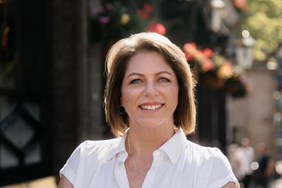 Brown haired woman outside, smiling, wearing white top