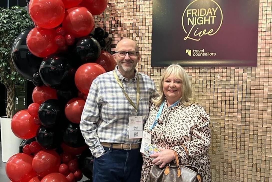 White man and white woman smiling at corporate party, balloons in the background