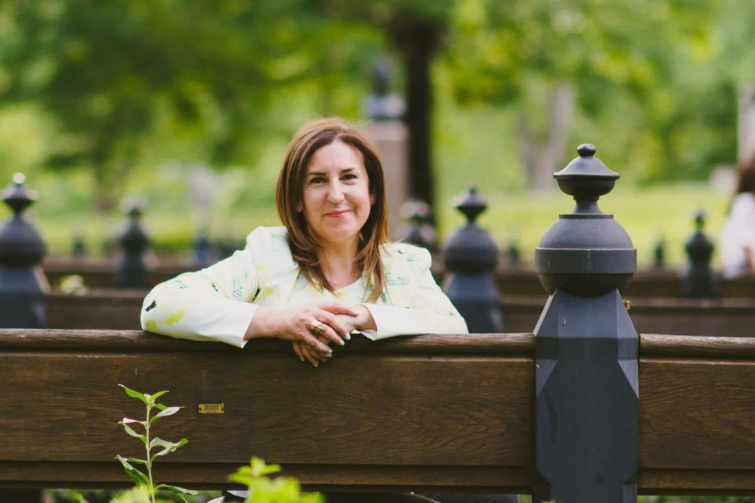 Woman with brown hair smiling and leaning against a railing, green background