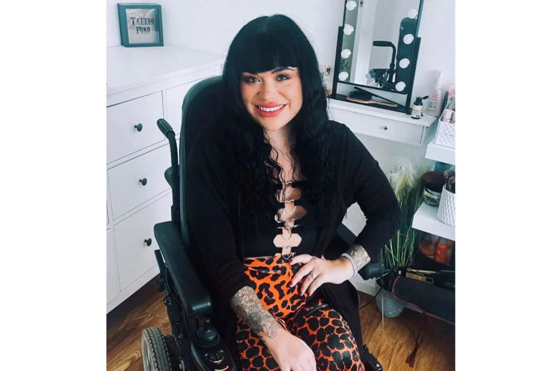White woman with shoulder-length black hair smiling, using wheelchair, office background