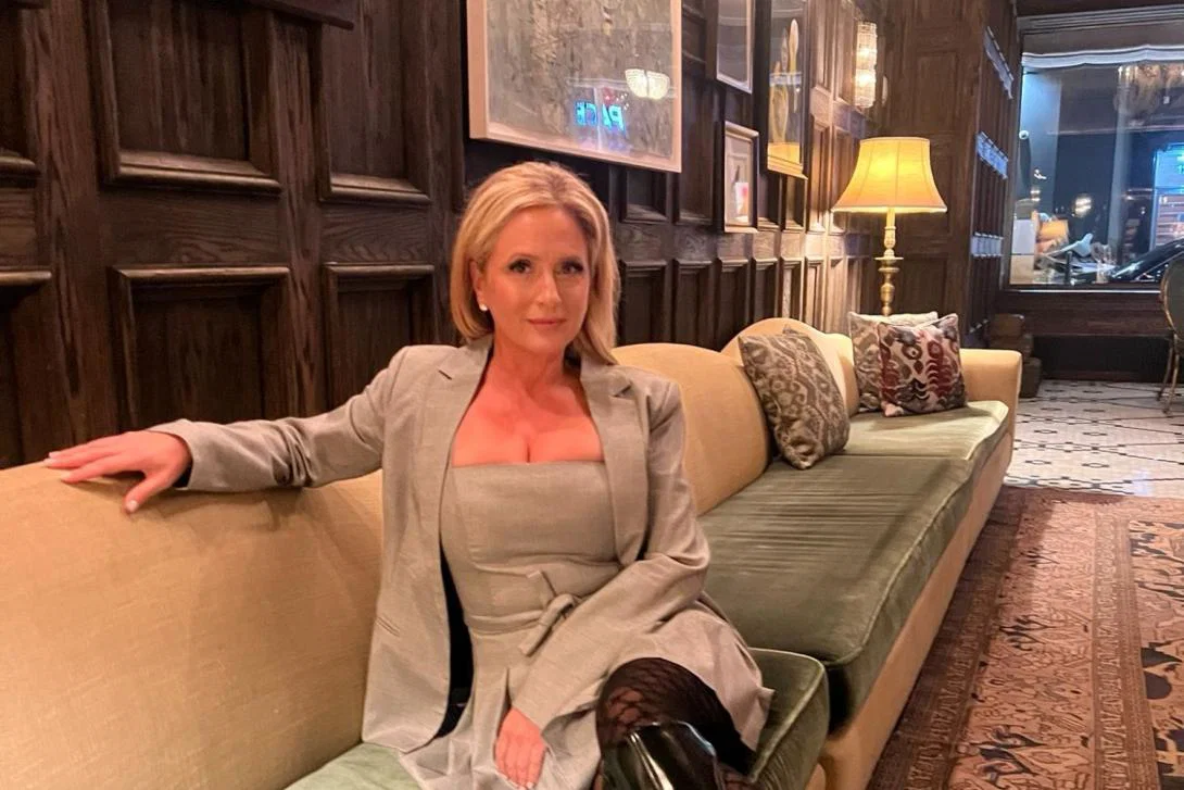 Woman with long blonde hair sitting on a sofa, looking serious