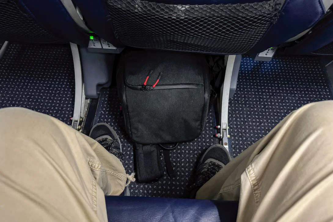 A carry-on bag pictured placed underneath the seat in front of the passenger