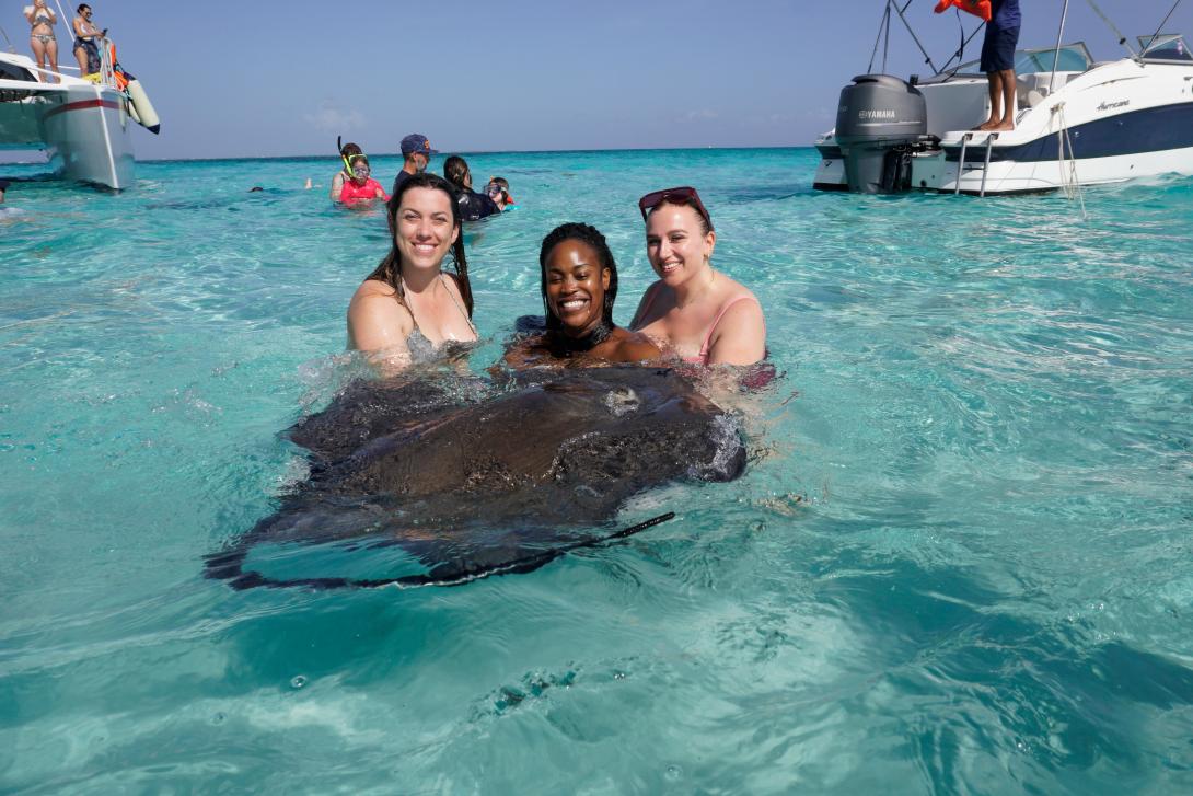 Three women smiling with a stingray in the sea