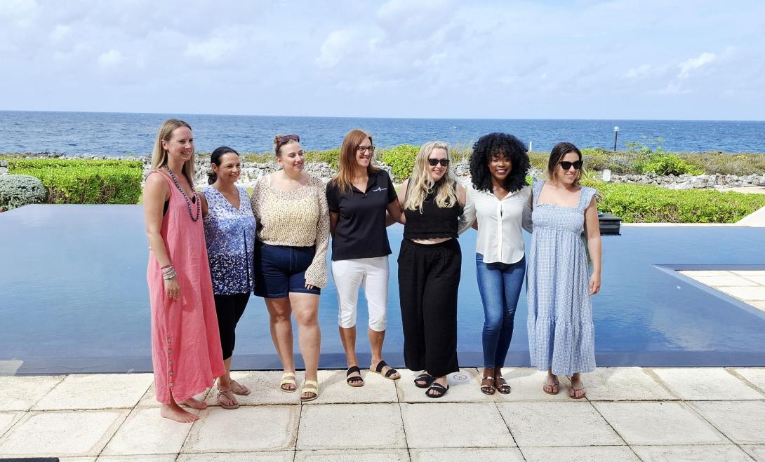 Seven women smiling and standing in front of a pool