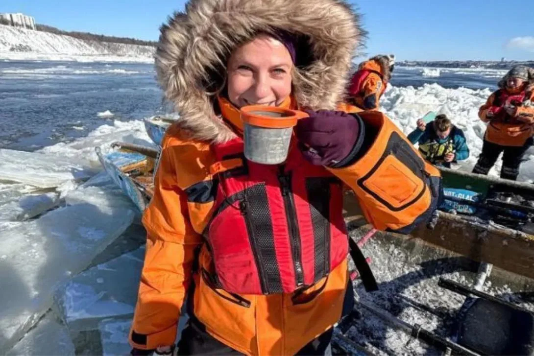 Woman wearing orange parka in snowy environment and sipping drink
