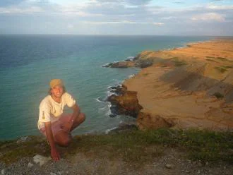 Charlie Thomas crouches in front of coastal scenery 